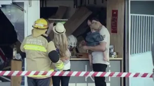 Firefighters assist a family after an incident at a storefront, with debris visible and safety tape in the foreground.