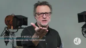 Man demonstrating mobile device photography techniques with studio lighting and cameras in the background.