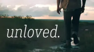 Person walking away on a path at sunset, with the word "unloved" displayed prominently in the foreground.