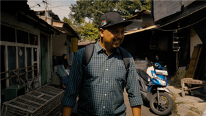 Person walking in a vibrant alley, showcasing local architecture and a parked blue motorcycle on a sunny day.
