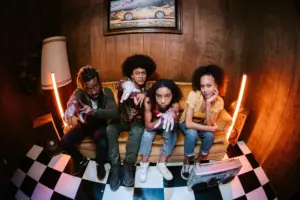 Four friends posing on a vintage couch in a retro-themed room with neon lighting and a checkered floor.