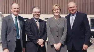 Four professionals posing together outdoors, dressed in business attire, showcasing a collaborative and cheerful atmosphere.