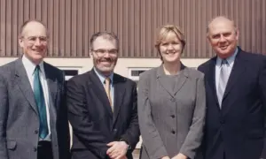 Four professionals smiling together outdoors in front of a building, dressed in formal attire, showcasing teamwork and leadership.