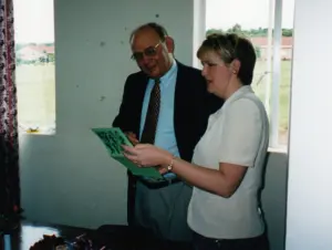 Two professionals discussing documents by a window, with papers in hand and a view of greenery outside.