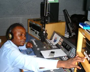 Radio host adjusting sound equipment in a studio, wearing headphones and focused on production tasks.