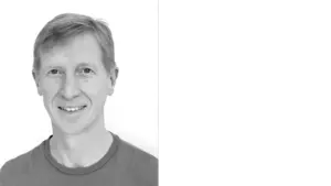 Smiling man in a red shirt against a white background, showcasing a friendly and approachable demeanor.