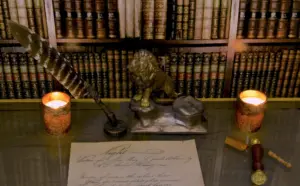 Quill, lion statue, and candles on a desk with vintage books in the background, creating an elegant study atmosphere.