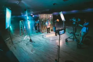 Film set with colorful lighting, crew preparing for a shoot, and backdrop, highlighting a creative production environment.