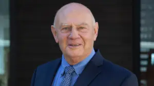 Smiling older man in a suit, standing outdoors with a blurred background, radiating warmth and confidence.