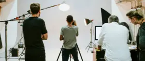 Photographers and crew working in a studio with lighting equipment and a backdrop, capturing a subject on camera.