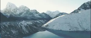 Stunning aerial view of snow-capped mountains reflecting in a serene alpine lake under a clear sky.