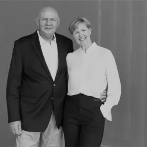 Smiling couple in formal attire, standing together against a neutral backdrop, showcasing a warm and welcoming demeanor.