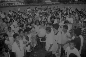 Black and white image of a large crowd of children and adults gathered around a globe in an outdoor setting.