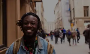 Smiling young man with headphones in a lively urban street filled with people, showcasing a vibrant, bustling city atmosphere.