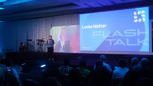 A speaker presents at a conference, with a vibrant stage backdrop and attentive audience engaged in a Flash Talk session.